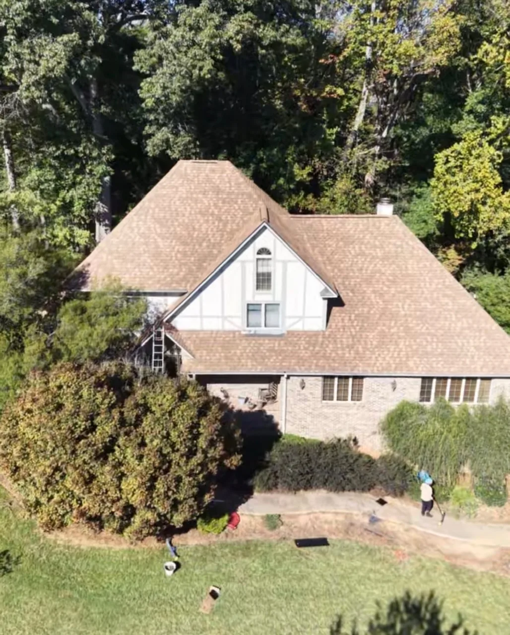 Aerial view of a home with a new tan shingle roof and crew cleaning up below